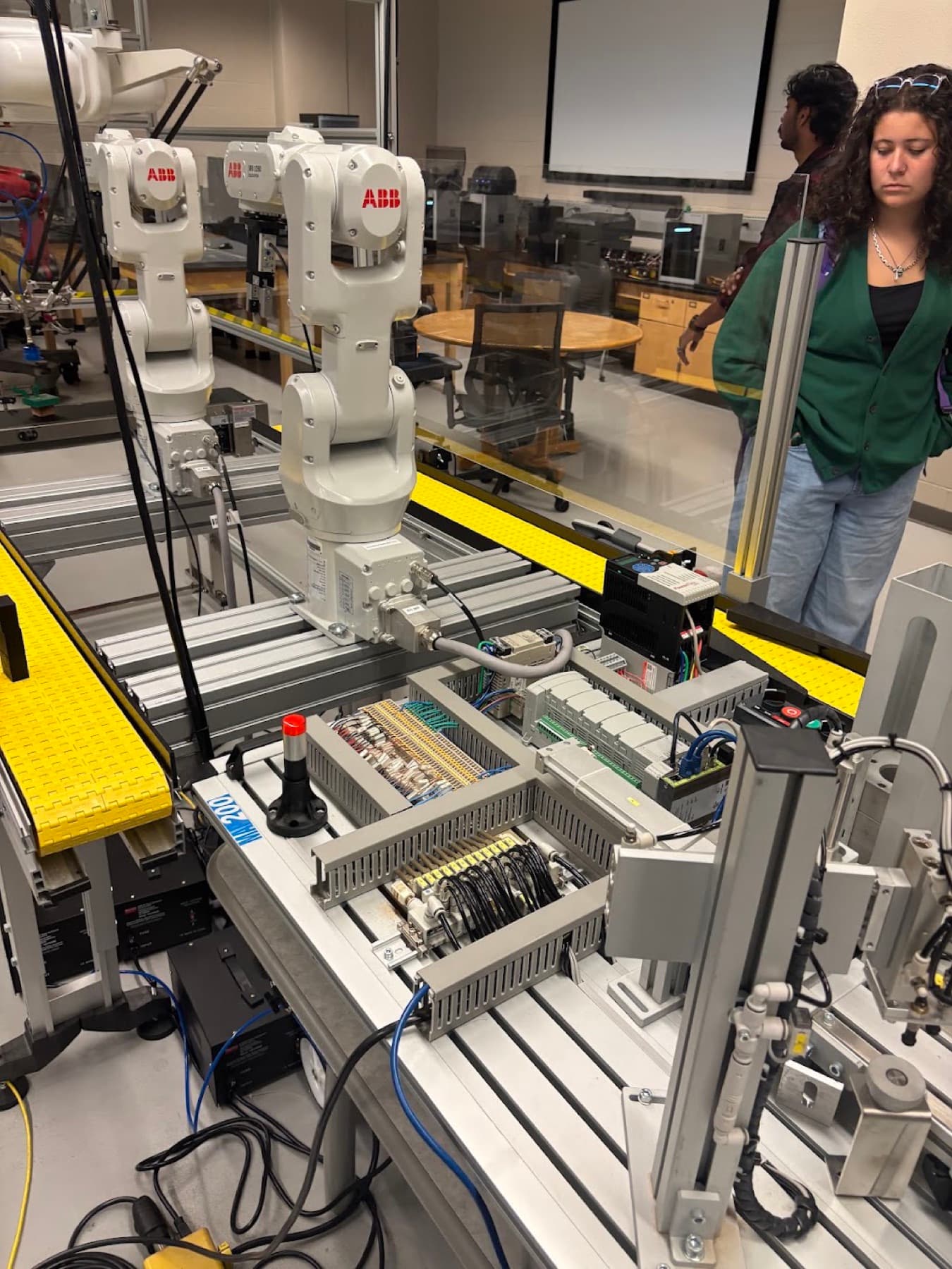 ABB robot arms over a conveyor with PLC wiring in the automation lab